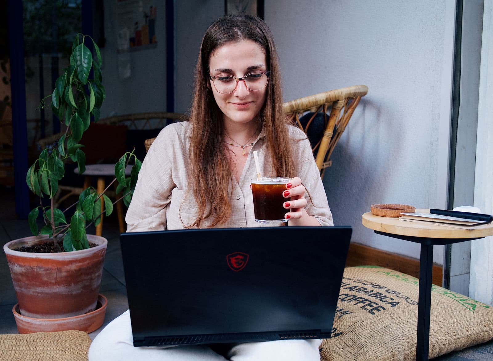 Une femme souriante, un café à la main, devant son ordinateur portable